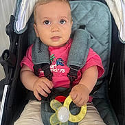 Luken participe au concours pour gagner de l'argent avec cette photo : baby, child, stroller, pacifier, toy, pink_shirt, shorts, curious_eyes, seatbelt, comfort, cute, person, infant, hand, face, summer_clothing, baby_toy, sitting, indoor, closeup