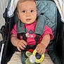 baby, child, stroller, pacifier, toy, pink_shirt, shorts, curious_eyes, seatbelt, comfort, cute, person, infant, hand, face, summer_clothing, baby_toy, sitting, indoor, closeup