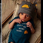 Gabriel joined the competition — help win amazing prizes! apparel, baby, blanket, child, cozy, cushion, cute, hat, headwear, indoor, infant, lying_down, onesie, person, portrait, soft_lighting, taco_design, text_on_clothing, wide_eyes, wood_floor