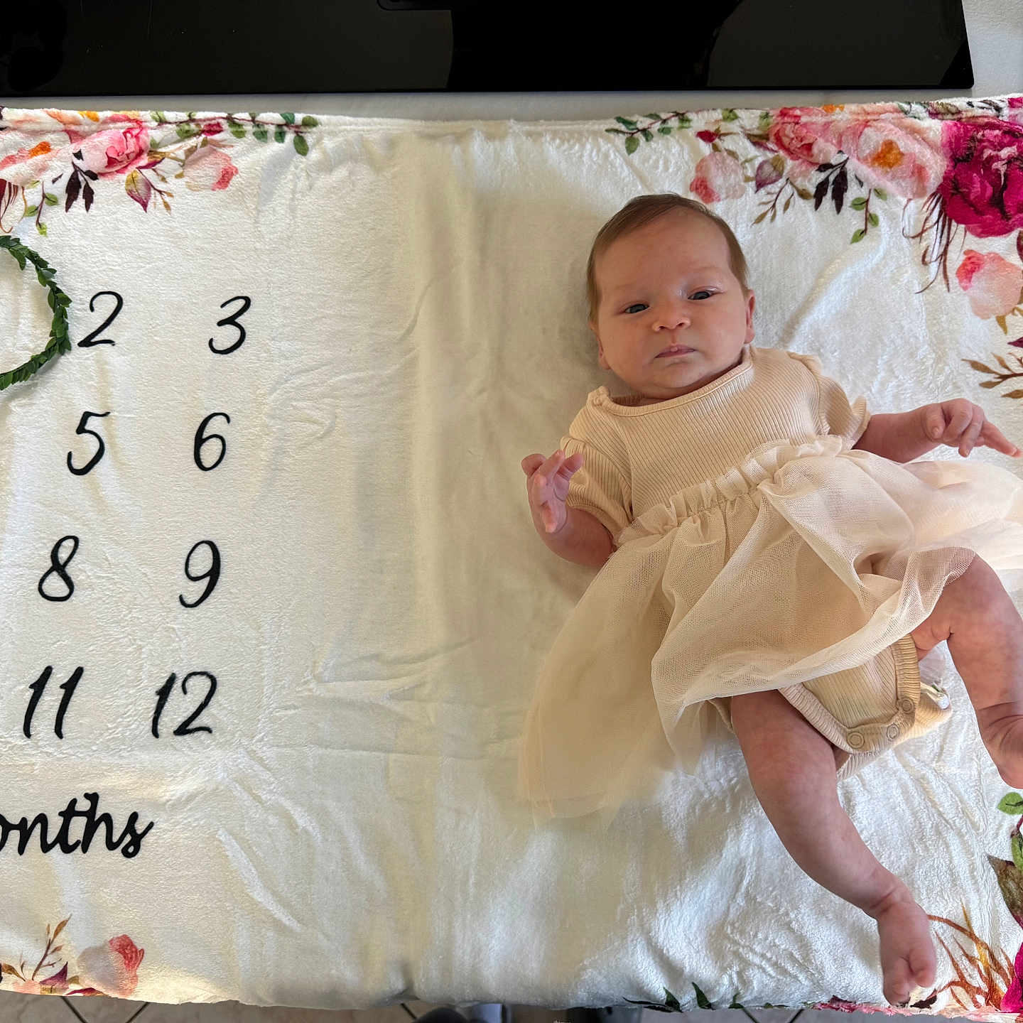 Emmé a rejoint le concours — aidez-le/la à gagner de superbes lots ! baby, blanket, celebration, child, cute, dress, floral, foot, hand, indoors, infant, laying, milestone, months, newborn, pattern, person, skin, soft, wreath