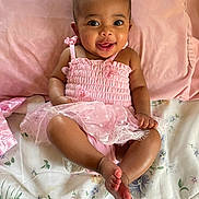 Amariah is registered to the contest to win money with this photo: baby, child, smiling, pink_dress, infant, lying_down, cute, happy, face, skin, pillow, blanket, fabric, indoors, person, toddler, foot, hand, head, eyes