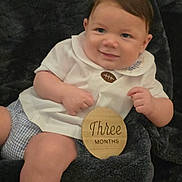 Waylon joined the competition — help win amazing prizes! baby, infant, three_months, white_shirt, checkered_shorts, wooden_sign, smiling, face, arms, legs, blue_eyes, brown_hair, blanket, soft_texture, milestone, portrait, indoors, cute, child, person