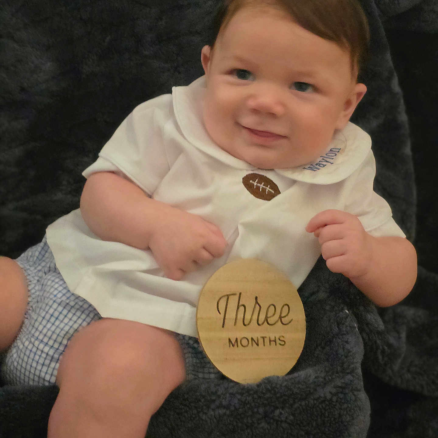 Waylon joined the competition — help win amazing prizes! arms, baby, blanket, blue_eyes, brown_hair, checkered_shorts, child, cute, face, indoors, infant, legs, milestone, person, portrait, smiling, soft_texture, three_months, white_shirt, wooden_sign