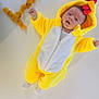 baby, infant, costume, yellow, chicken, animal_costume, dried_apricots, fruit, number_seven, white_background, cute, lying_down, soft_texture, hooded_outfit, child, portrait, expression, playful, food_arrangement, indoor