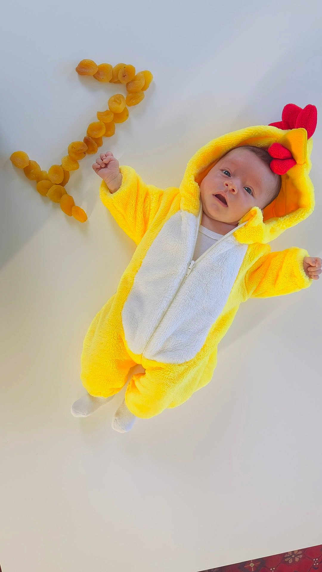 Liza a rejoint le concours — aidez-le/la à gagner de superbes lots ! baby, infant, costume, yellow, chicken, animal_costume, dried_apricots, fruit, number_seven, white_background, cute, lying_down, soft_texture, hooded_outfit, child, portrait, expression, playful, food_arrangement, indoor