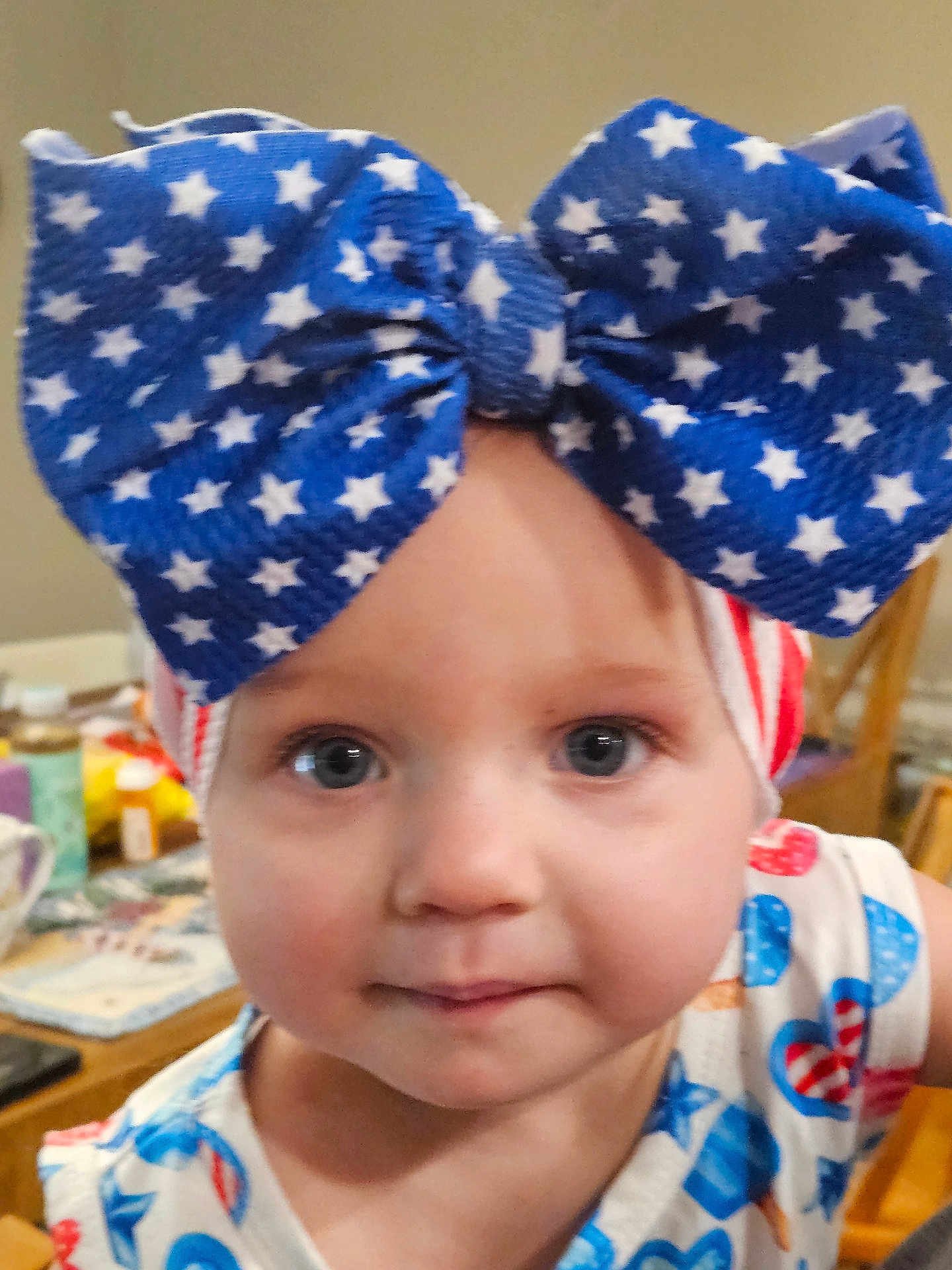 Prudence is registered to the contest to win money with this photo: baby, blue_bow, chair, child, closeup, clothing, curious, cute, expression, face, headband, indoor, patterned_clothing, person, portrait, red_white_blue, star_pattern, table, toddler, young_child