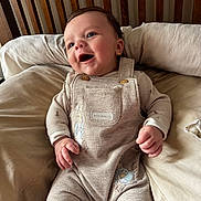 Luca joined the competition — help win amazing prizes! baby, smiling, infant, overalls, peter_rabbit, cushion, bed, clothing, cute, happy, child, portrait, indoors, soft, comfortable, young, person, sitting, face, wooden_headboard