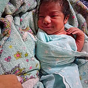 Miguel joined the competition — help win amazing prizes! newborn, baby, blanket, swaddle, smile, lying_down, quilt, patterned_blanket, infant, soft_texture, cute, child, wrapped, bed, cozy, hand, face, peaceful, indoors, resting