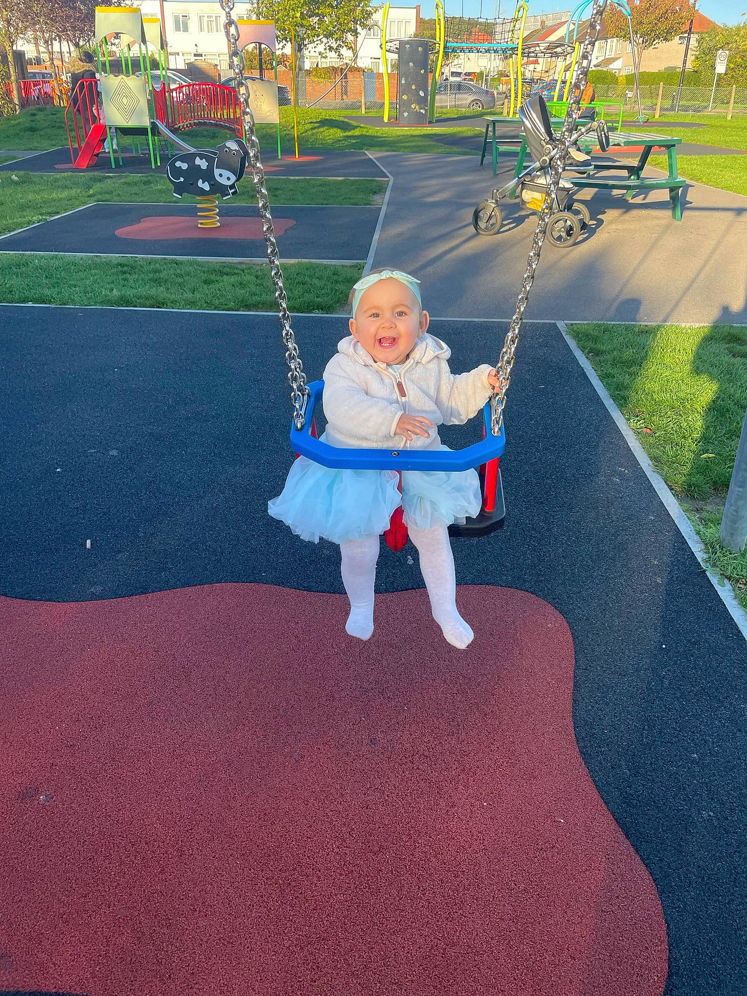 Bonnie is registered to the contest to win money with this photo: asphalt, baby, child, city, electric_blue, flooring, fun, grass, headwear, leisure, outdoor_play_equipment, person, plant, play, playground, pole, recreation, road_surface, sitting, swing