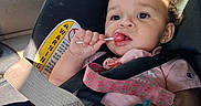Tirzah is registered to the contest to win money with this photo: baby, child, car_seat, car, lollipop, candy, smiling, portrait, indoor, vehicle, seatbelt, safety_harness, curly_hair, pink_clothing, earring, pacifier, window, sky, sunlight, close_up