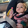 baby, child, infant, car_seat, car, safety_harness, seatbelt, lollipop, pacifier, curly_hair, smiling, portrait, sitting, indoors, vehicle, pink_clothing, earring, sunlight, road_trip, safety_sign