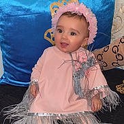 Eline a rejoint le concours — aidez-le/la à gagner de superbes lots ! baby, child, sitting, pink_clothing, headband, feathers, flowers, shoes, sparkly, couch, pillow, blue_pillow, smiling, happy, indoors, portrait, cute, young_child, fashion, accessories