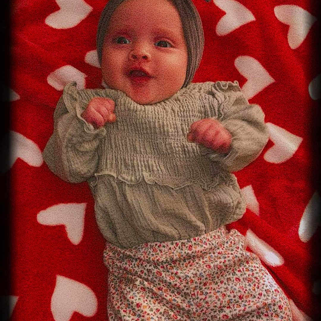 Saraphina joined the competition — help win amazing prizes! baby, infant, headband, bow, blanket, hearts, red, white, clothing, patterned_pants, cute, lying_down, portrait, child, small_hands, smiling, vignette, cozy, soft_texture, happy