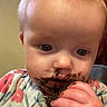 baby, child, face, messy, food, chocolate, hand, indoor, clothing, floral_pattern, curious, close_up, infant, portrait, young_child, cute, holding, eating, messy_face, person