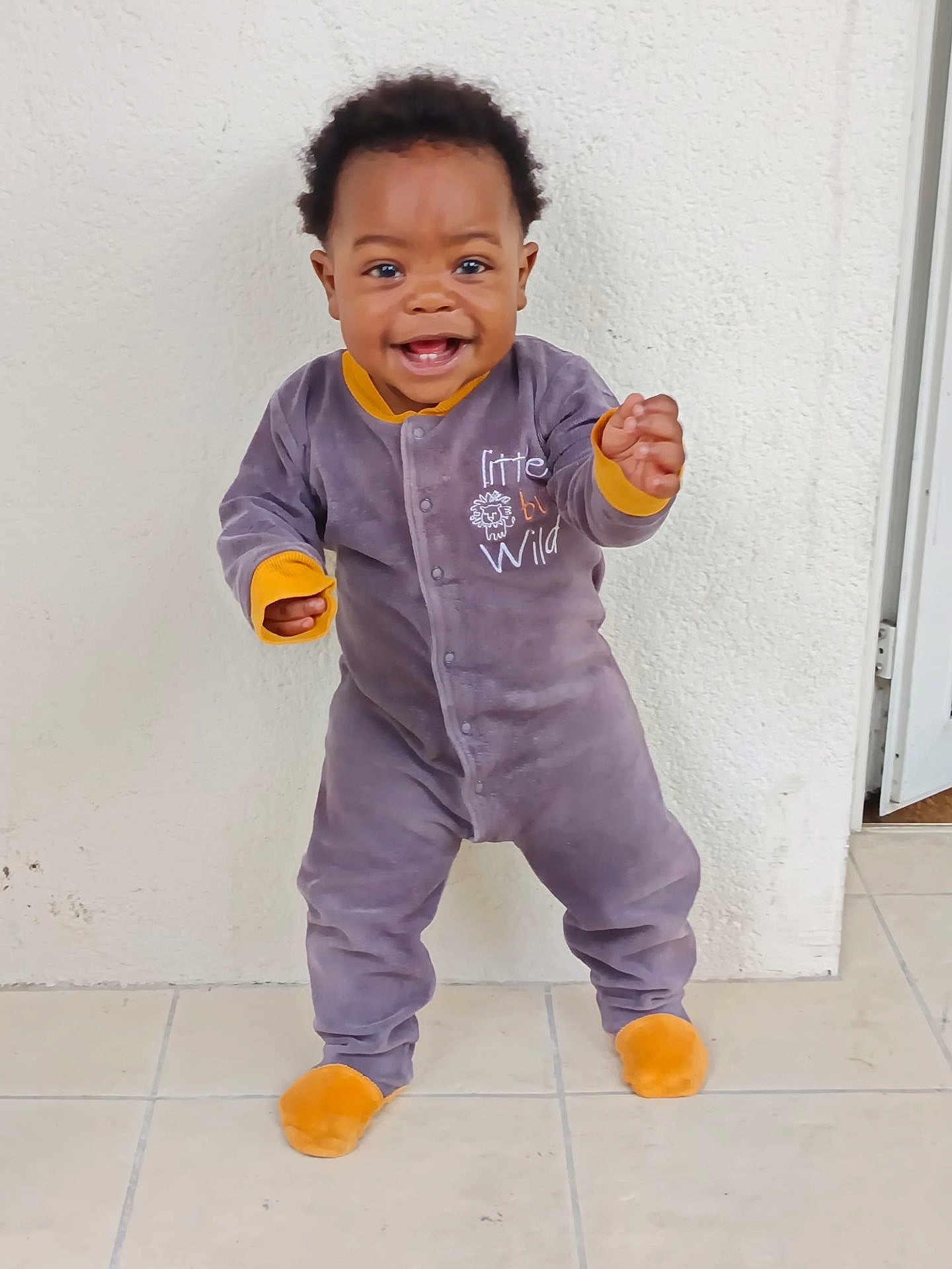 Ravi Manuel participe au concours pour gagner de l'argent avec cette photo : baby, child, onesie, smiling, standing, floor, tile, wall, indoor, happy, cute, person, infant, clothing, footwear, face, expression, young, portrait, playful