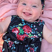 Jaylee is registered to the contest to win money with this photo: baby, smiling, tongue_out, headband, floral_dress, pink_blanket, close_up, child, happy, cheeks, cute, infant, portrait, skin, eyes, person, laying_down, clothing, fashion, soft_texture