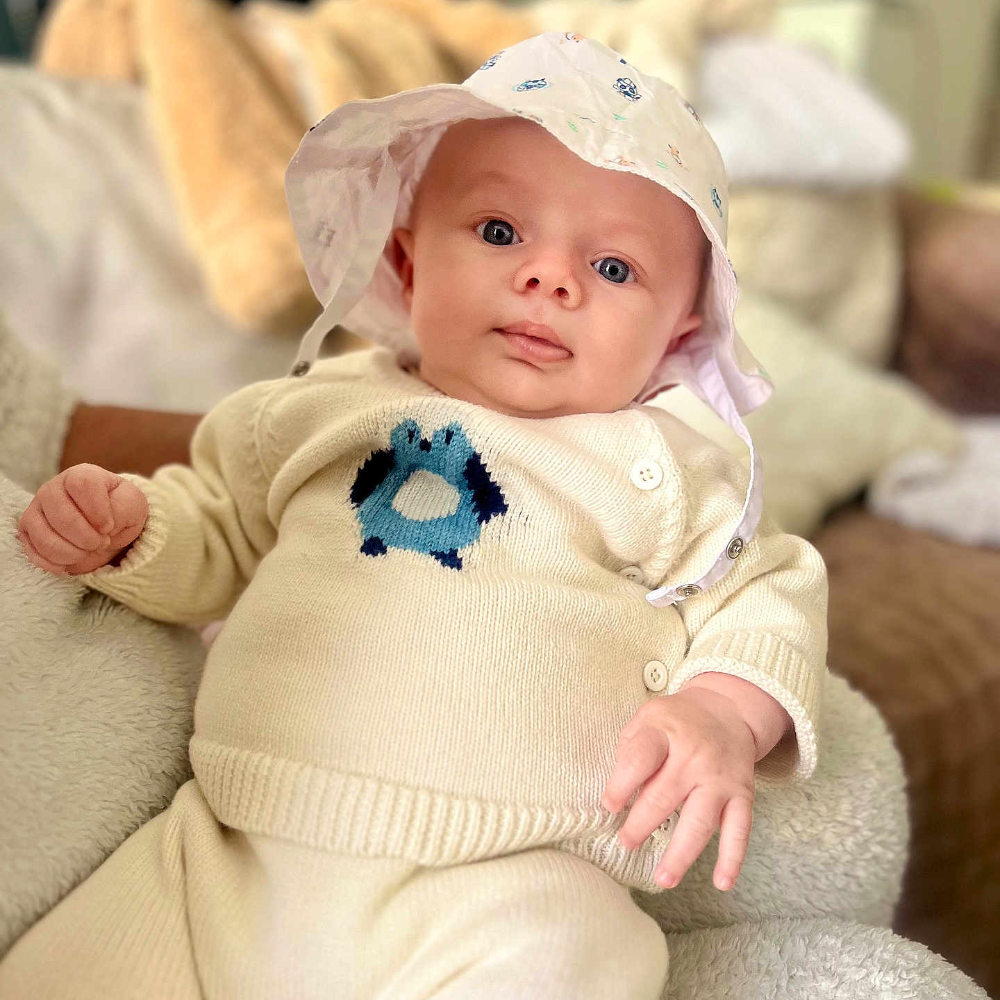 Léo a rejoint le concours — aidez-le/la à gagner de superbes lots ! baby, child, hat, knitwear, cream_color, cushion, indoor, portrait, cute, infant, soft_texture, comfortable, relaxed, person, apparel, closeup, smiling, face, hand, seated