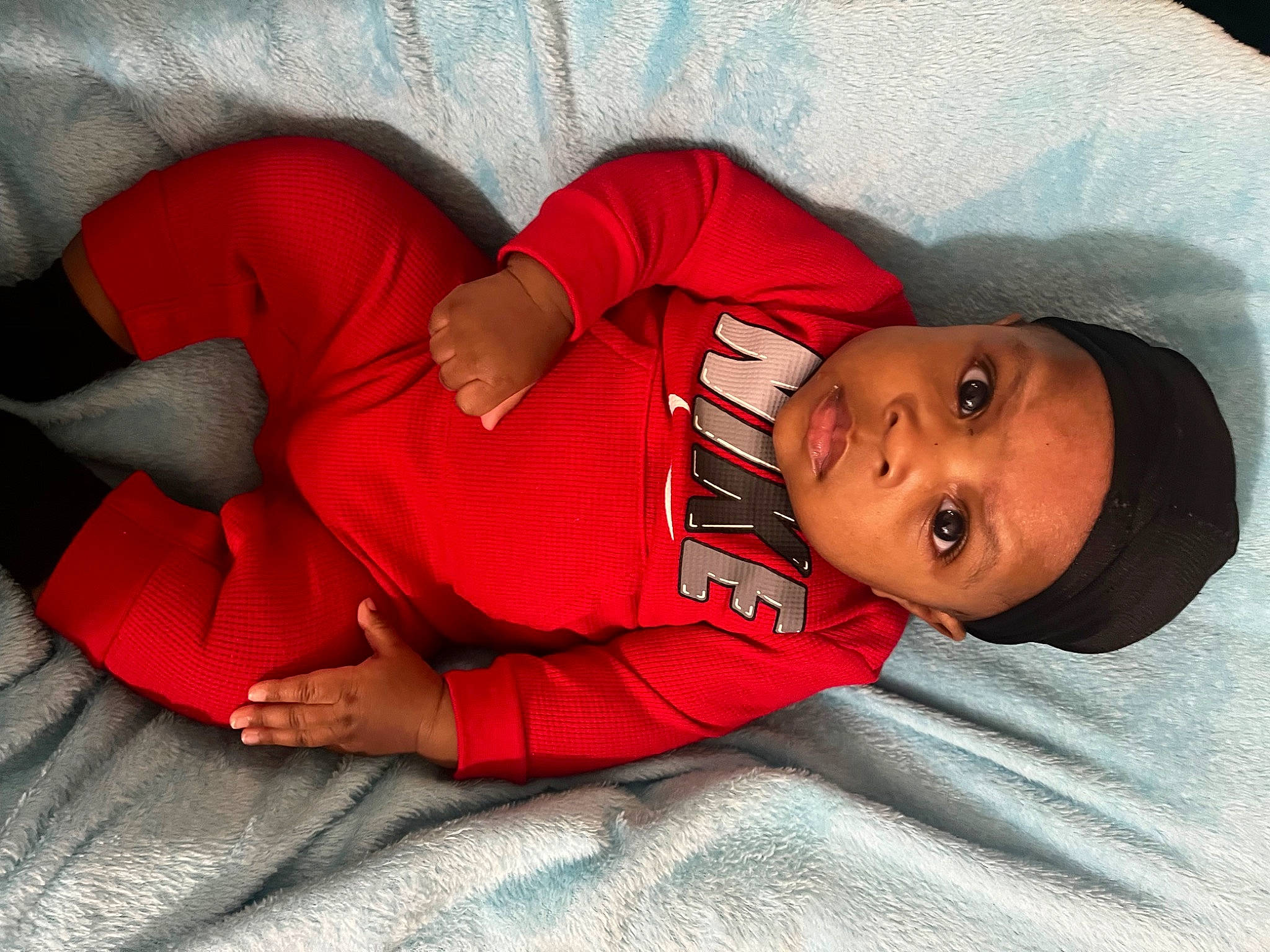 Harlem is registered to the contest to win money with this photo: baby, baby_sleeping, baby_toddler_clothing, carmine, child, comfort, elbow, eye, face, head, headwear, human_leg, knee, linens, magenta, person, red, skin, sleeve, thigh