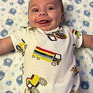 Michael is registered to the contest to win money with this photo: baby, infant, smiling, tongue_out, onesie, truck_print, blanket, teddy_bear_pattern, lying_down, happy, cute, child, playful, indoors, carpet, light_skin, short_hair, portrait, young_child, expressive_face