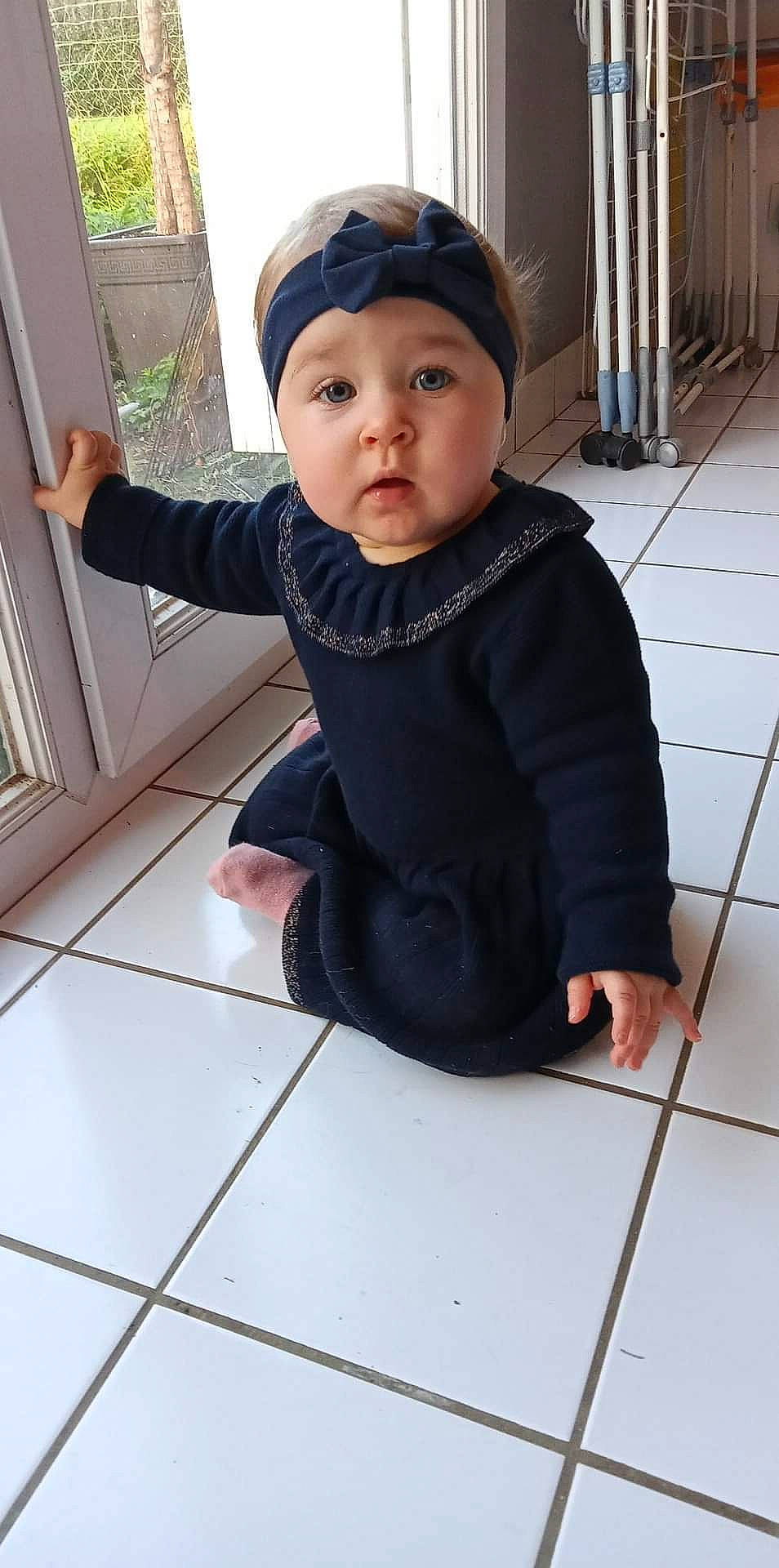 Louna participe au concours pour gagner de l'argent avec cette photo : baby, baby_toddler_clothing, beanie, cap, cheek, child, concrete, fashion_accessory, floor, flooring, fur, headwear, pattern, person, sitting, sleeve, surprise, t_shirt, toddler, window