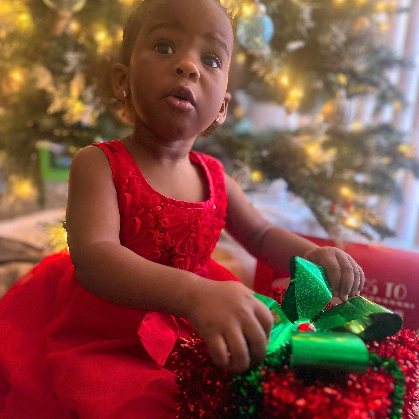 Trinity is registered to the contest to win money with this photo: child, christmas, christmasdecorations, christmastree, clothing, dress, face, female, festival, gift, girl, happy, head, openingpresent, person, photography, plant, portrait, sitting, smile