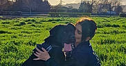 Mia a rejoint le concours — aidez-le/la à gagner de superbes lots ! dog, person, human, outdoor, field, grass, sunset, sunlight, sky, clouds, power_lines, pylon, countryside, cuddle, hugging, sitting, black_dog, pet, portrait, nature