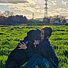 dog, person, human, outdoor, field, grass, sunset, sunlight, sky, clouds, power_lines, pylon, countryside, cuddle, hugging, sitting, black_dog, pet, portrait, nature
