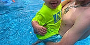 Aiden is registered to the contest to win money with this photo: child, toddler, man, swimming_pool, water, outdoor, summer, smiling, tongue_out, playful, holding, family, fun, casual, bright_clothing, necklace, water_splash, backyard, trees, house