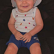 Aiden is registered to the contest to win money with this photo: toddler, child, smiling, hat, bucket_hat, sleeveless_shirt, stars_pattern, shorts, blue_shorts, sitting, couch, indoor, happy, portrait, face, hands, legs, closeup, casual_clothing, person