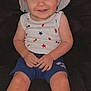 toddler, child, smiling, hat, bucket_hat, sleeveless_shirt, stars_pattern, shorts, blue_shorts, sitting, couch, indoor, happy, portrait, face, hands, legs, closeup, casual_clothing, person