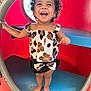 toddler, child, smiling, curly_hair, barefoot, playground, play_equipment, red_tunnel, blue_seat, clothing, top, shorts, bow, happy, joyful, outdoor, person, standing, cute, laughing