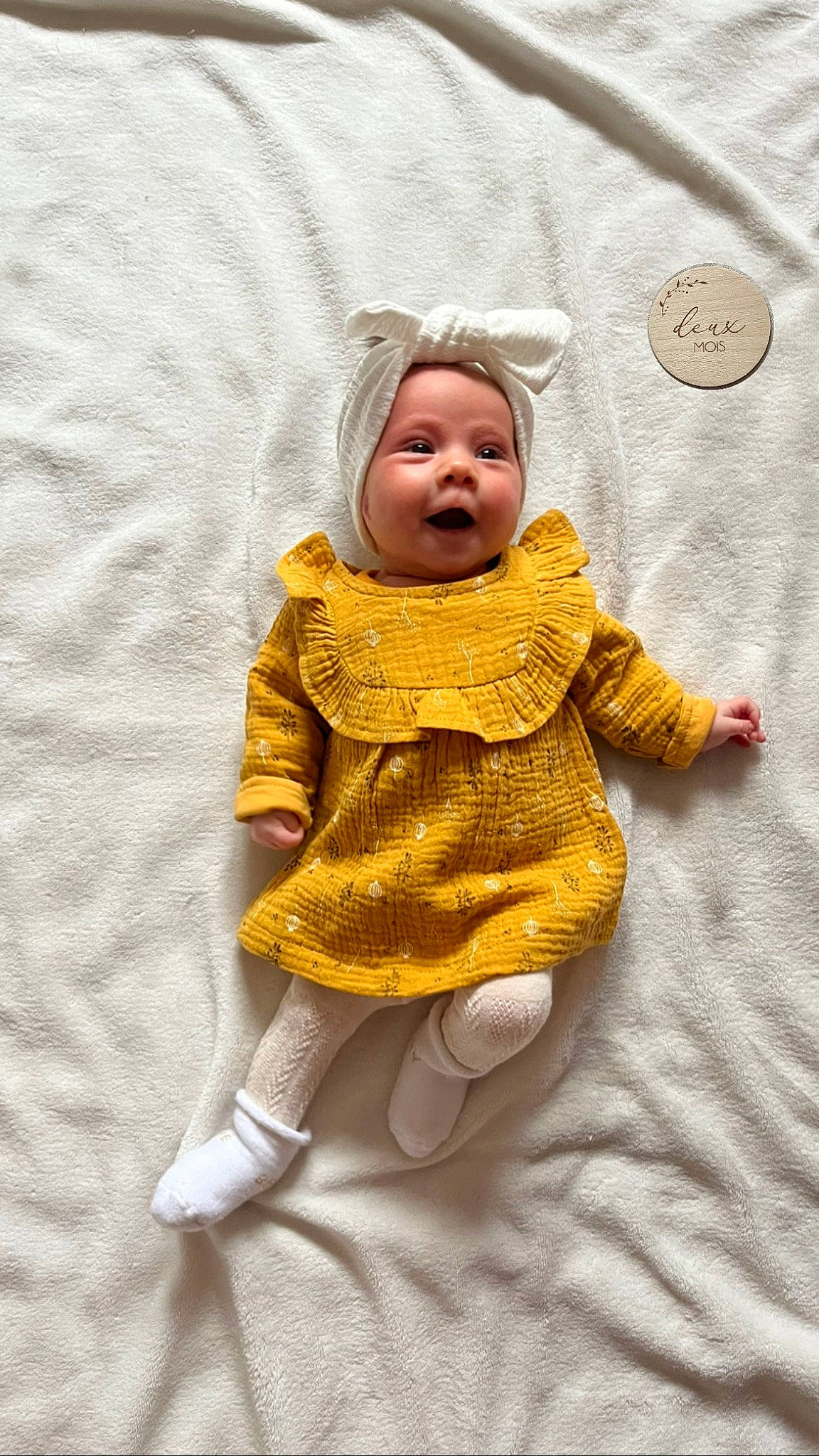 Mila participe au concours pour gagner de l'argent avec cette photo : baby, baby_toddler_clothing, cheek, child, comfort, dress, eye, face, happy, head, headgear, headwear, linens, outerwear, pattern, person, skin, sleeve, smile, textile