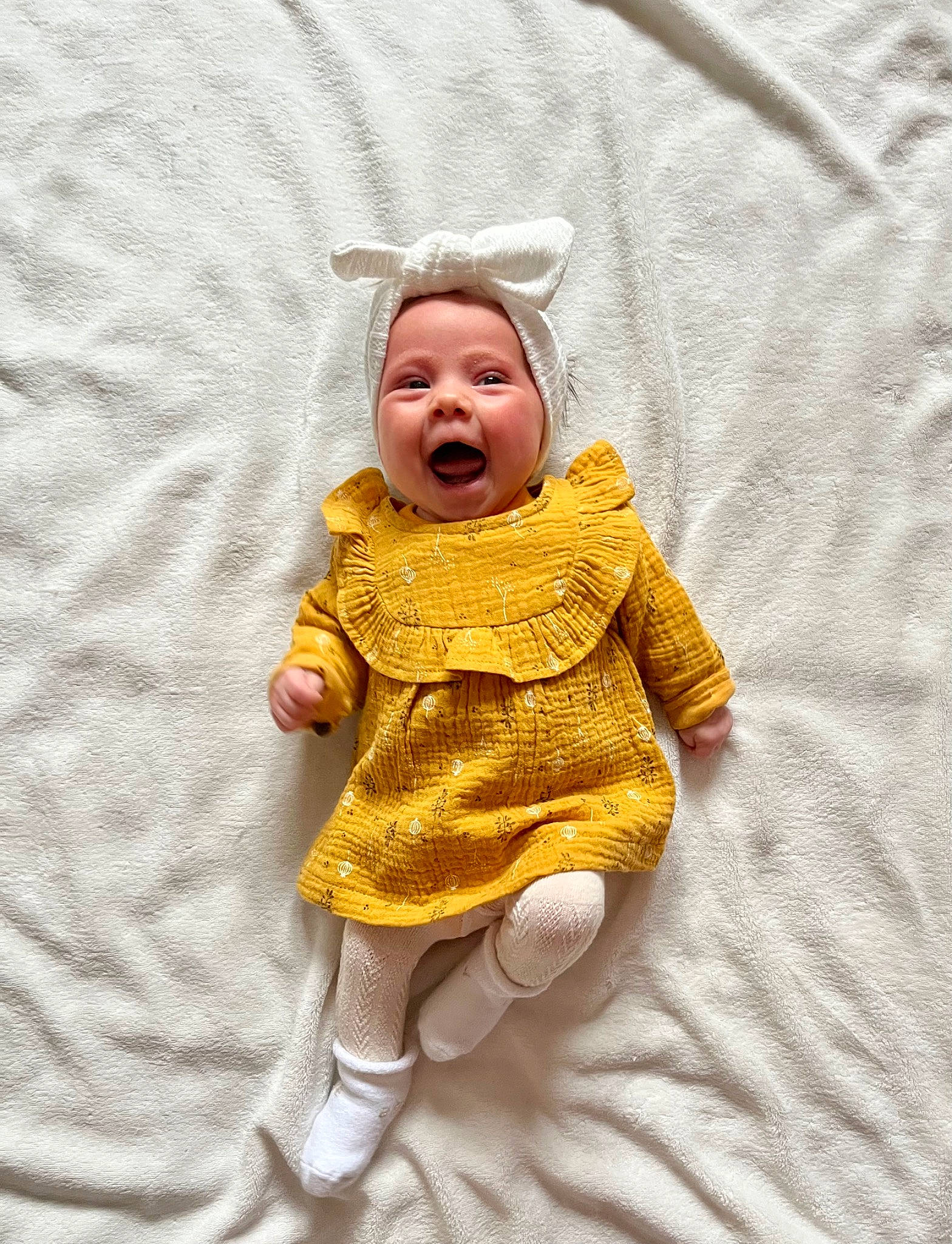 Mila participe au concours pour gagner de l'argent avec cette photo : arm, baby, baby_products, baby_toddler_clothing, cheek, comfort, dress, eye, face, gesture, happy, head, headgear, headwear, linens, pattern, person, sleeve, smile, textile