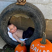 Dallas is registered to the contest to win money with this photo: baby, tire, pumpkin, painted_pumpkin, footprints, outdoor, grass, wall, antlers, child, shirtless, jeans, smile, face, head, nature, decoration, fall, autumn, cute