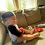 Dallas is registered to the contest to win money with this photo: toddler, child, couch, toy, snack, window, curtains, sippy_cup, light, indoor, clothing, face, legs, barefoot, sitting, beige, black, red, plastic, home