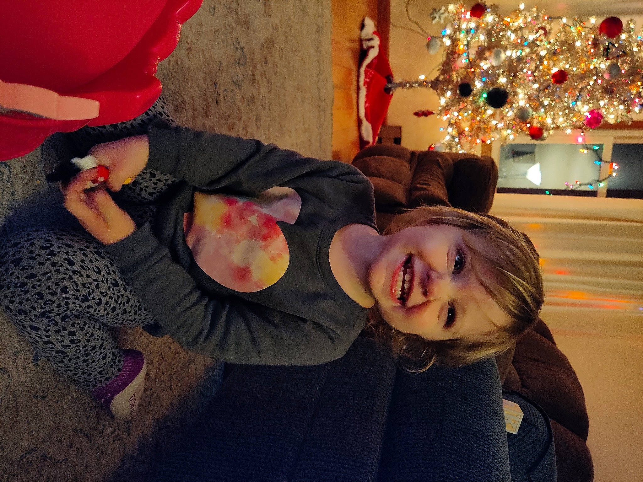 Malayah is registered to the contest to win money with this photo: child, christmas, christmas_decoration, christmas_eve, christmas_ornament, christmas_tree, event, fun, gesture, happy, holiday, human_leg, joy, lap, leisure, person, room, sitting, smile, toddler