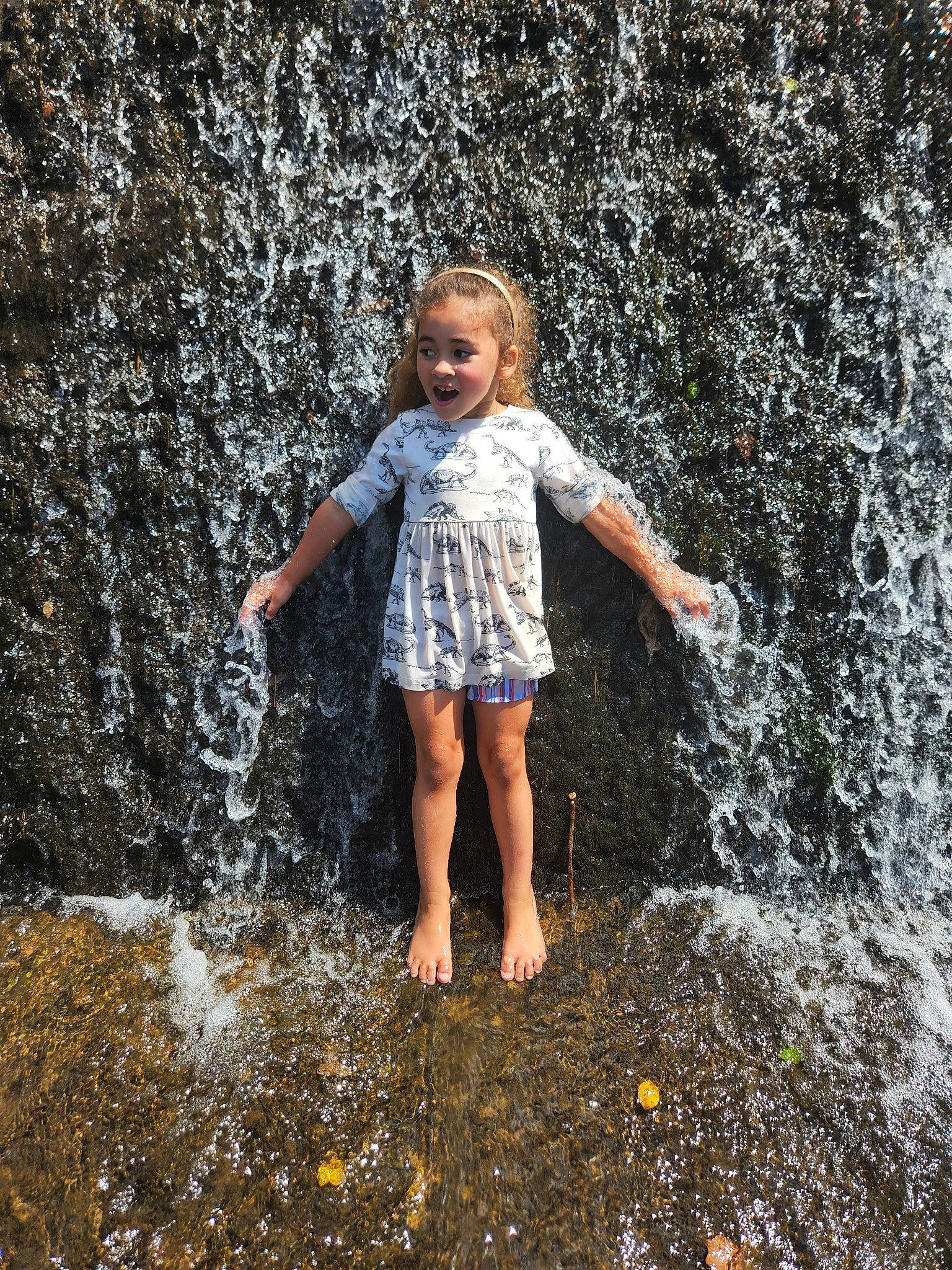 Lillian is registered to the contest to win money with this photo: asphalt, barefoot, flash_photography, fountain, fun, grass, happy, human_leg, leisure, long_hair, people_in_nature, person, road_surface, shoulder, sitting, summer, t_shirt, toddler, water, water_feature
