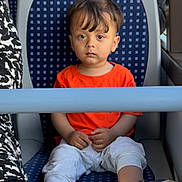 Azlan joined the competition — help win amazing prizes! toddler, child, orange_shirt, white_pants, blue_shoes, seat, public_transport, bus, serious_expression, sitting, safety_bar, sole_of_shoes, patterned_seat, indoor, person, young_child, casual_clothing, short_hair, daylight, travel