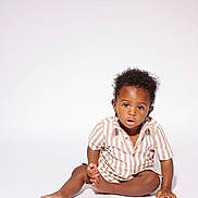 Carter is registered to the contest to win money with this photo: toddler, child, sitting, striped_shirt, curly_hair, white_background, studio, portrait, barefoot, casual_clothing, young_child, expression, face, person, indoor, isolated, fashion, cute, one_person, baby