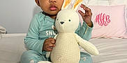 Mylani is registered to the contest to win money with this photo: baby, child, plush_toy, bunny, pajamas, bed, pillow, foot, hand, face, indoors, cute, soft_toy, person, sleepwear, infant, monogram, comfort, toy, cozy