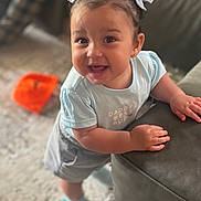 Isla Jo Alexander is registered to the contest to win money with this photo: toddler, child, smiling, happy, blue_clothing, hair_bows, indoors, carpet, couch, baby_shoes, cute, portrait, playful, leaning, young_child, person, face, expression, home, casual