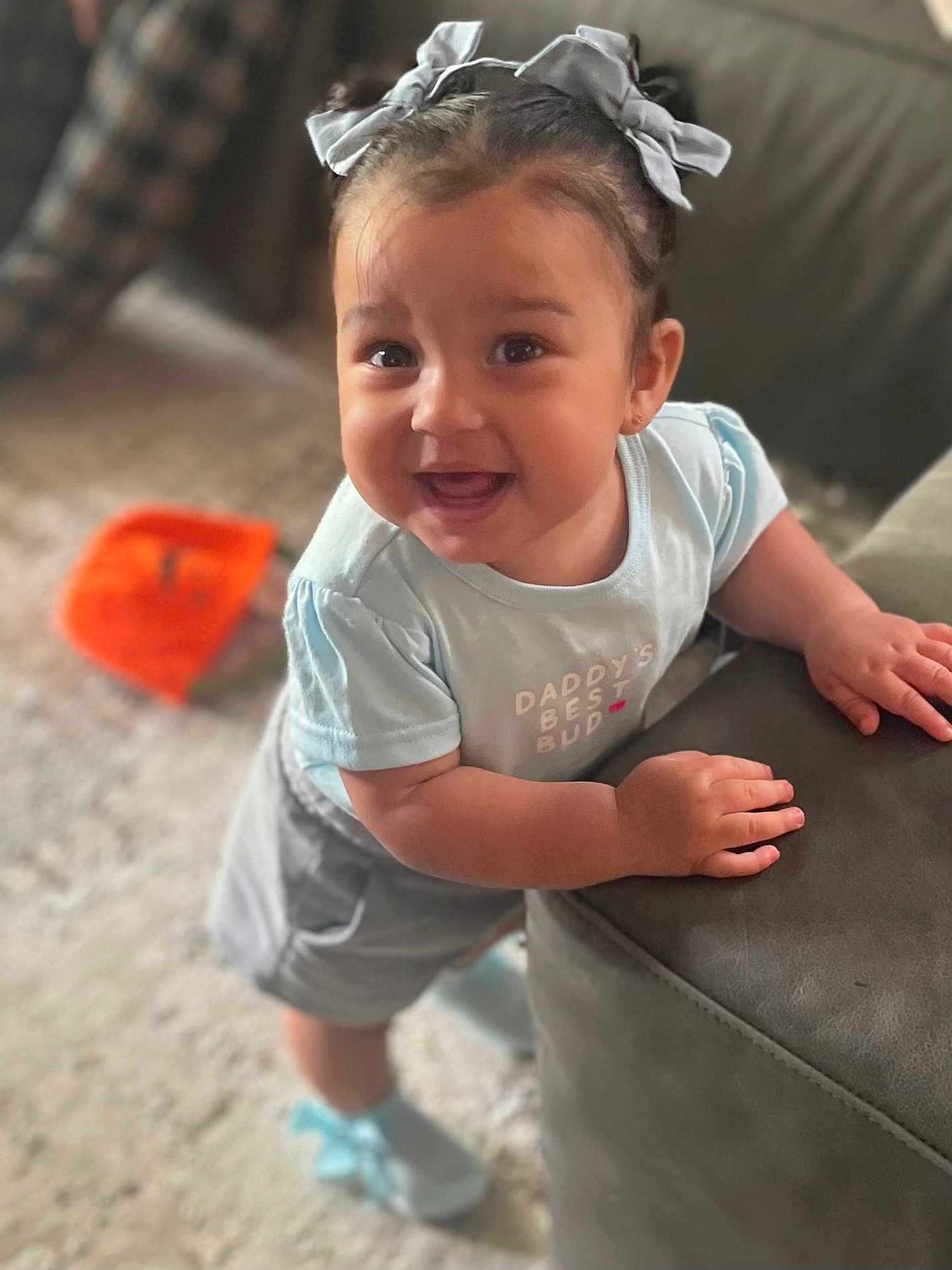 Isla Jo Alexander is registered to the contest to win money with this photo: toddler, child, smiling, happy, blue_clothing, hair_bows, indoors, carpet, couch, baby_shoes, cute, portrait, playful, leaning, young_child, person, face, expression, home, casual