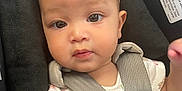 Evangeline is registered to the contest to win money with this photo: baby, child, car_seat, headband, bow, onesie, toy, straps, warning_label, seat_belt, infant, cute, face, eyes, hand, fabric, pattern, colorful, sitting, indoor