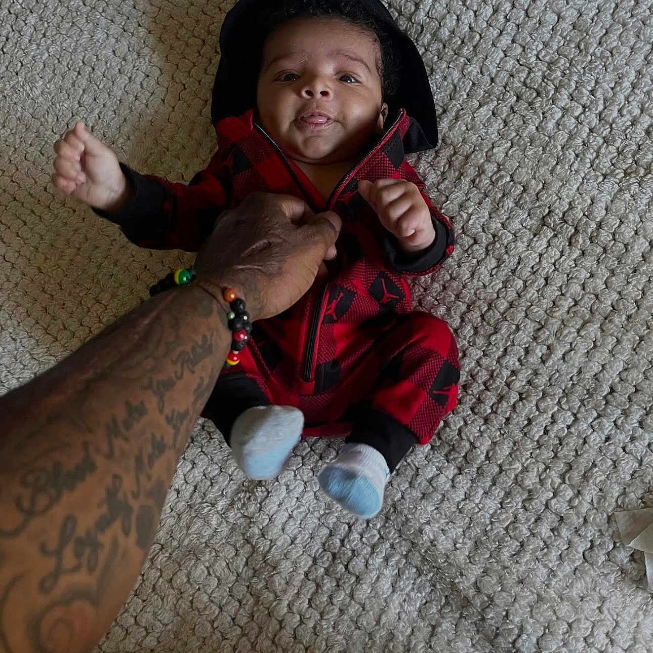 Kealo joined the competition — help win amazing prizes! baby, black_clothing, carpet, child, cute, floor, hand, holding, hoodie, human, indoor, infant, person, red_clothing, smile, socks, tattoo, texture, tongue_out, young_child