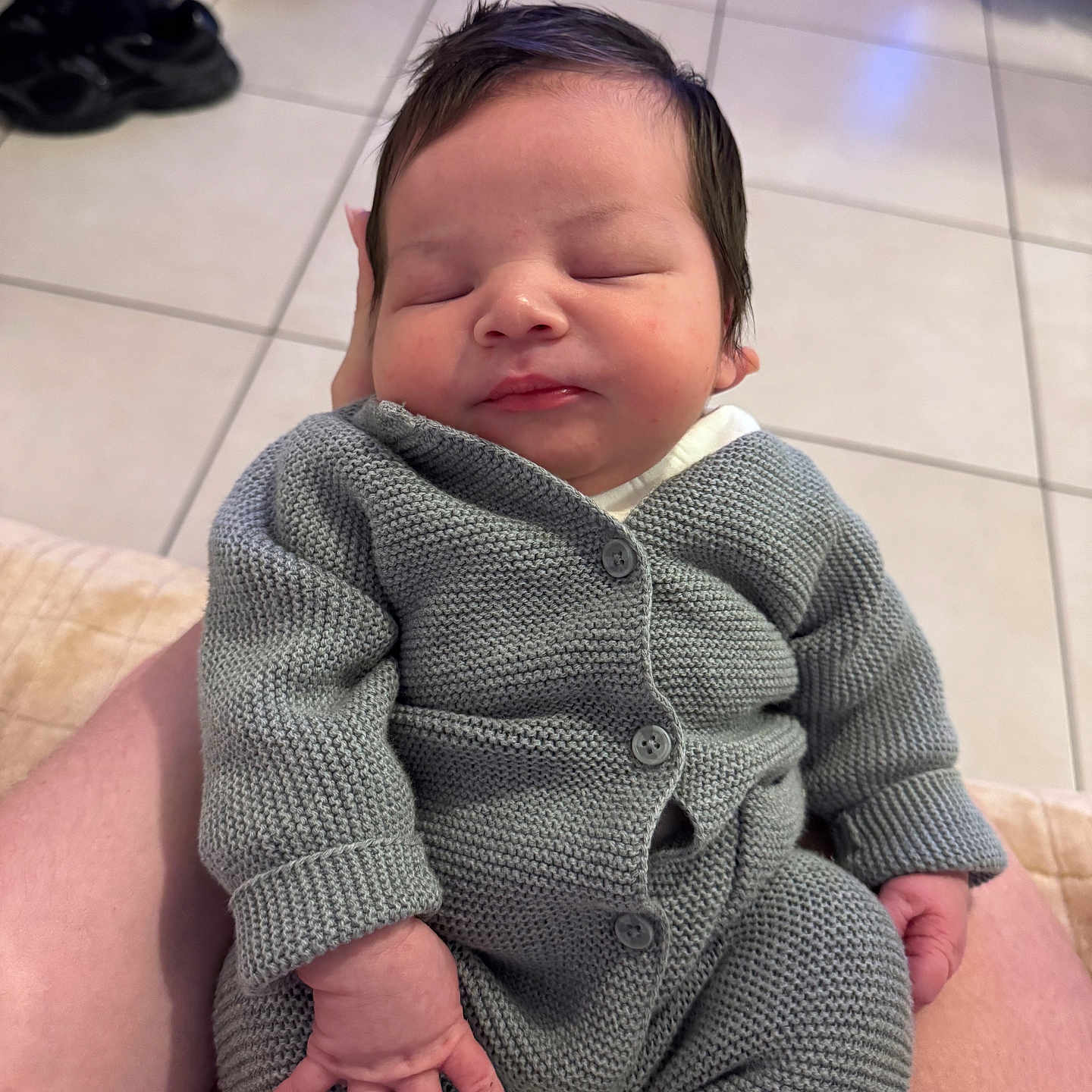 Layan a rejoint le concours — aidez-le/la à gagner de superbes lots ! baby, infant, sleeping, knitwear, gray_clothing, hand, footwear, tile_floor, indoor, person, resting, cute, soft_lighting, cozy, newborn, casual, relaxed, human, seated, portrait