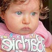 Izahbella is registered to the contest to win money with this photo: arm, baby, blue_eyes, casual, child, clothing, colorful_text, curly_hair, cute, expression, face, holding, human, indoor, person, pink_shirt, portrait, skin, toddler, young_child