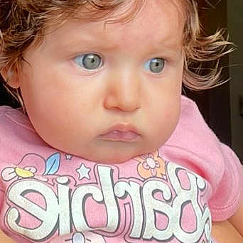 Izahbella is registered to the contest to win money with this photo: arm, baby, blue_eyes, casual, child, clothing, colorful_text, curly_hair, cute, expression, face, holding, human, indoor, person, pink_shirt, portrait, skin, toddler, young_child