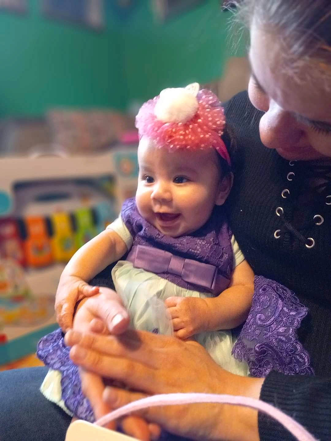 Aleena is registered to the contest to win money with this photo: baby, baby_toddler_clothing, cheek, child, doll, fashion_accessory, finger, fun, gesture, happy, head, headwear, iris, lip, person, pink, purple, sitting, skin, thumb