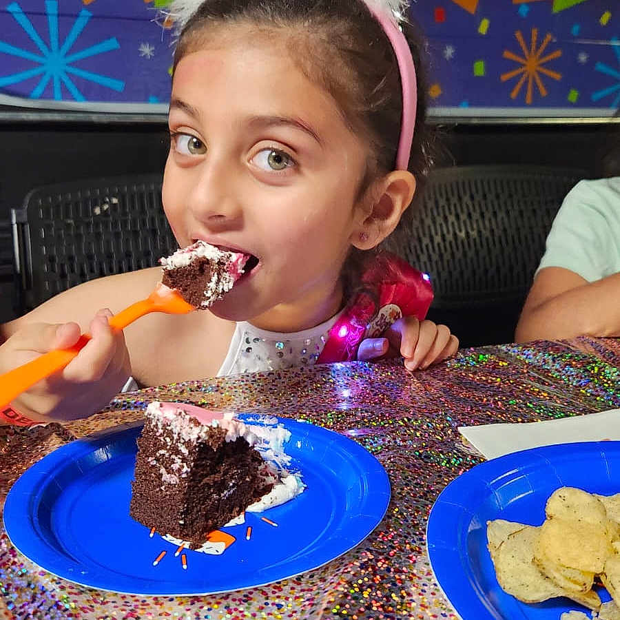 Inaaya is registered to the contest to win money with this photo: birthdaycake, child, clothing, cream, cutlery, dessert, eating, face, female, food, girl, hat, head, icing, people, person, photography, plate, portrait, spoon