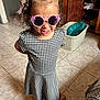 child, girl, sunglasses, dress, black_and_white, checkered, curly_hair, hair_tie, pink, indoors, floor, tile, smile, happy, footwear, sandals, laundry_basket, cabinet, home, person